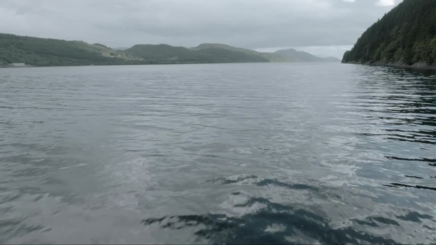 Water rippling on lake surrounded by mountains on cloudy day