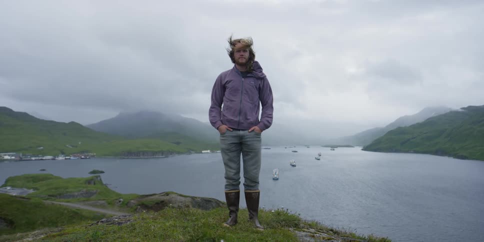 Man stands on a hill overlooking a bay as the wind blows