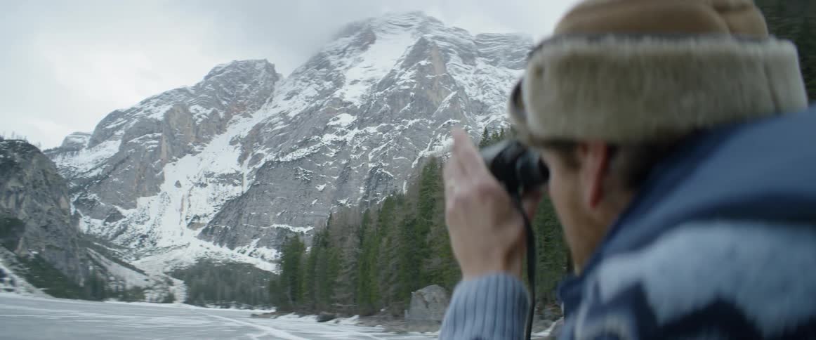 Woman holding a cigarette and a camera takes pictures of snowy mountains