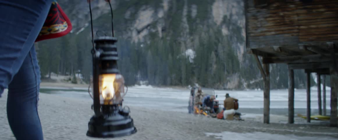 A woman carries a lantern near a mountain lake