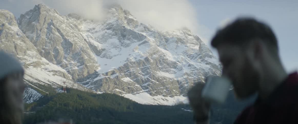 A man and woman are drinking coffee in front of a large mountain