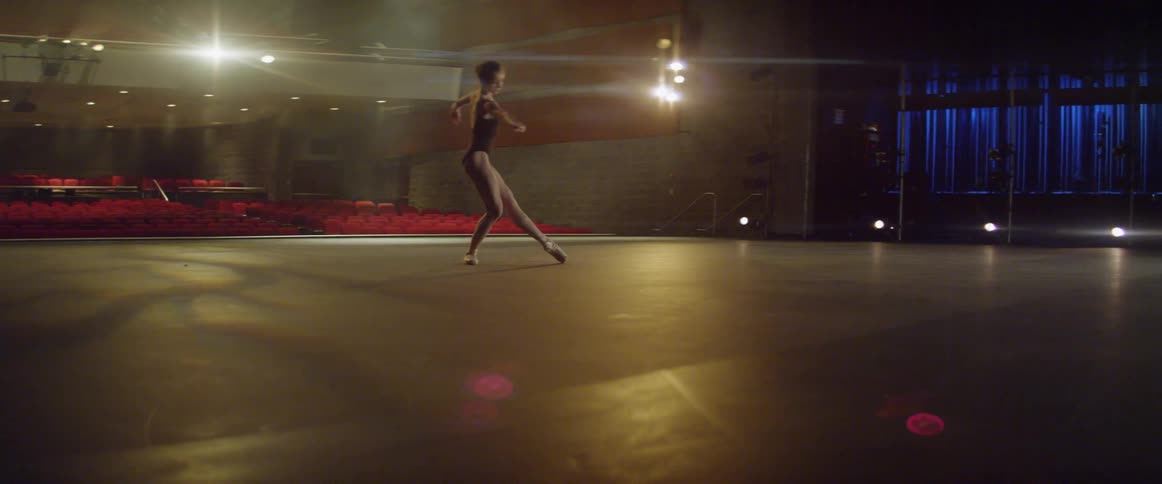 Young ballerina is spinning and dancing on stage in auditorium