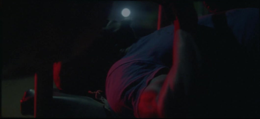 A male athlete is lying on a bench lifting weights outdoors at night
