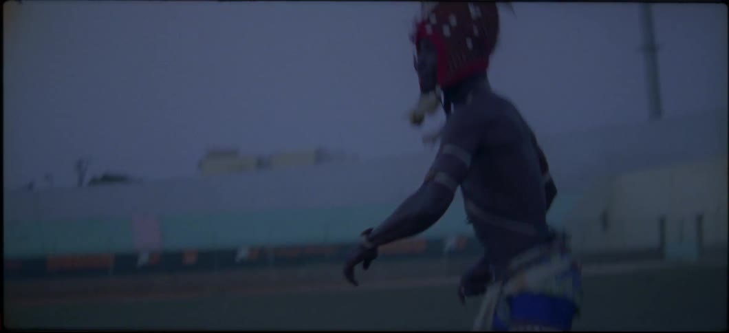 A man in a head dress is dancing and jogging through a stadium