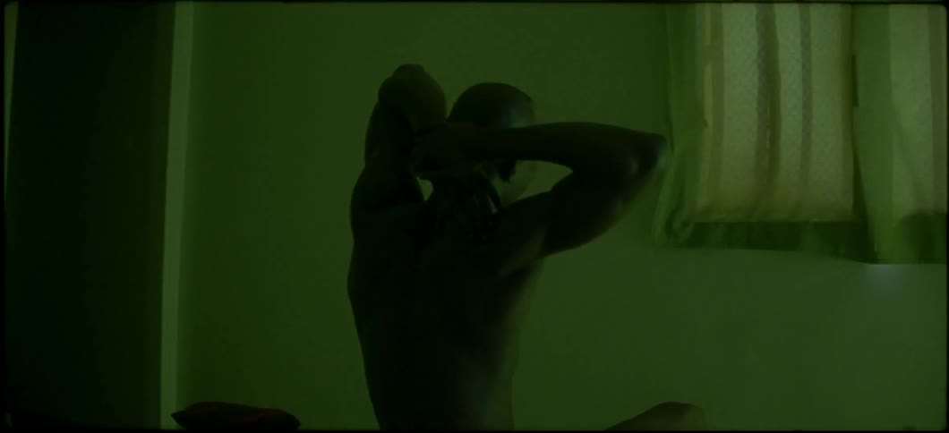 A man is sitting in a green lit room stretching