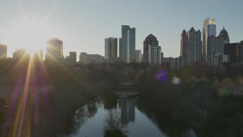 A view of a river leading towards a city while the sun glares from behind some buildings