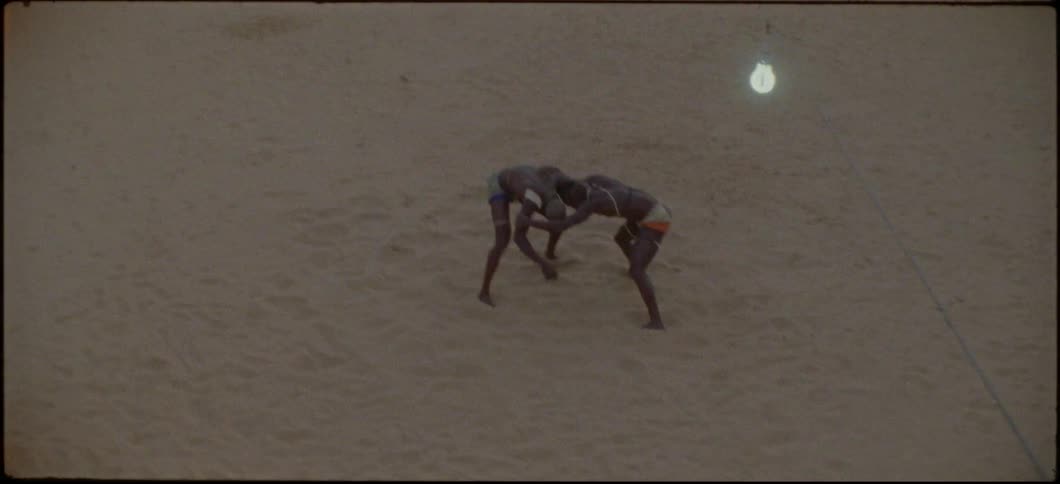 Two men wrestle on the beach