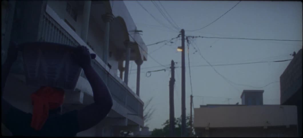 Person walks next to a building carrying a basket on their head