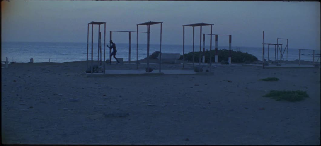 A man shadow boxes near workout equipment on the beach
