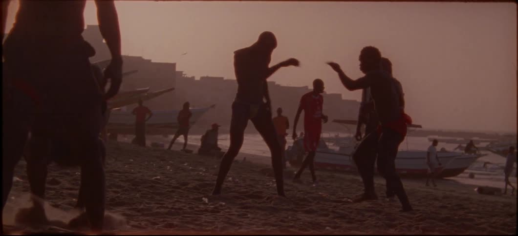 Two people spar as others walk on the beach