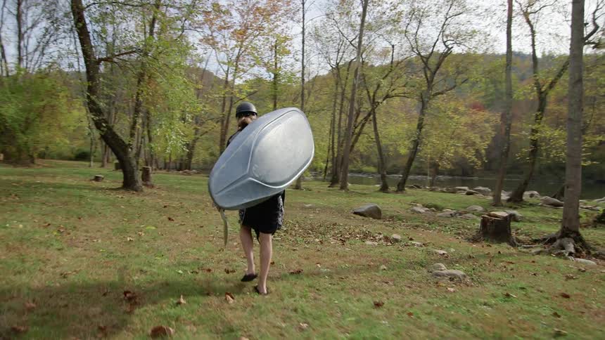 A person carries a kayak toward a river