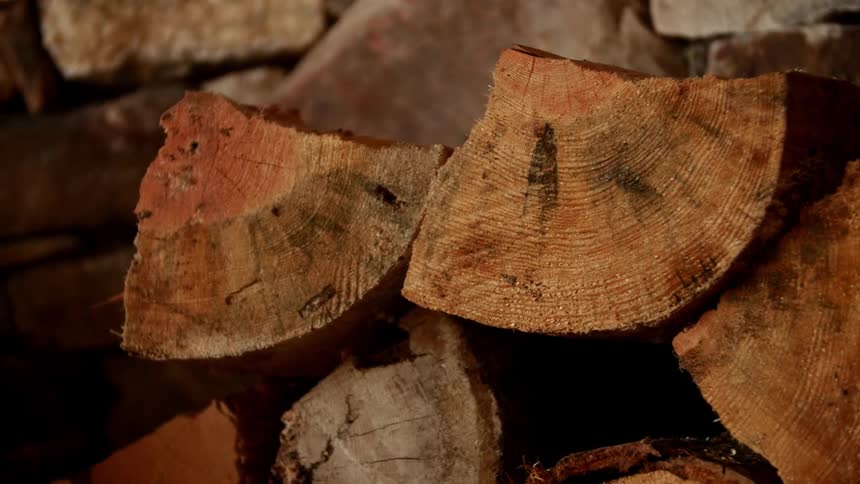 Split firewood is stacked against a stone wall