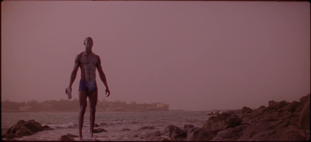 A man is standing on some rocks and pours liquid over his head