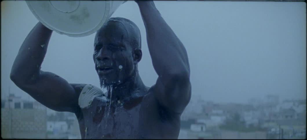 A shirtless man pours water from a bucket on his head