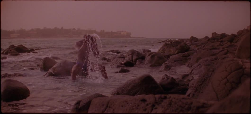 A man is sitting on a rock in the ocean and scooping water over his head