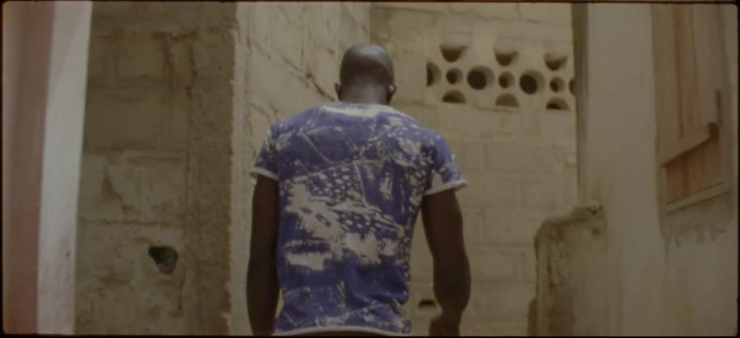 A man with headphones in is walking down a small alley