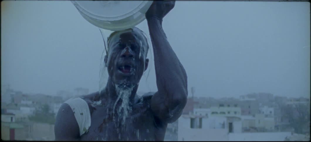 A man is dumping a bucket of water over his head on a rooftop