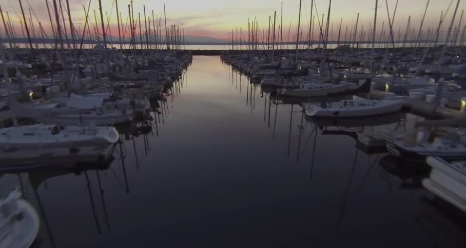 The sun setting on rows of sail boats in a marina
