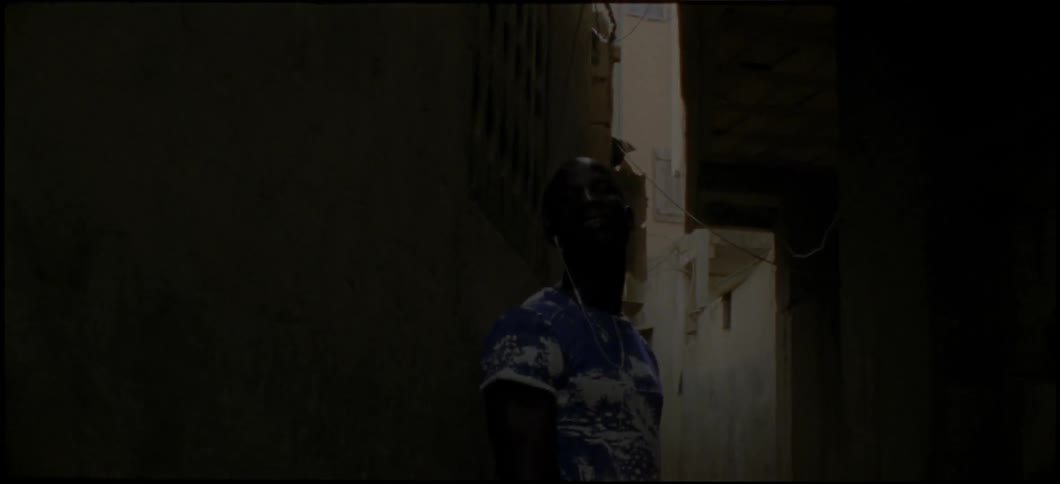 A man in a blue shirt walks through a narrow alley