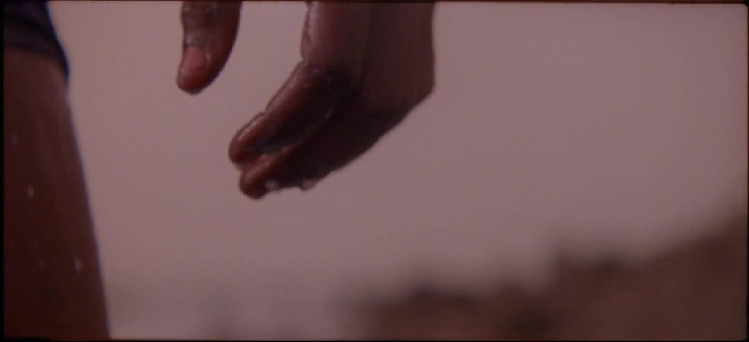 Water drips from a man's hand as he stands outside at sunset
