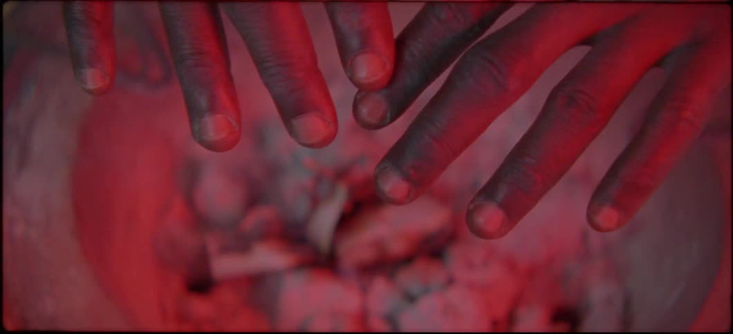 A man warms his hands over a smoking fire