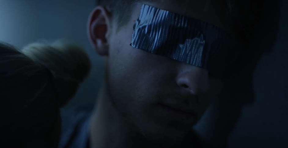 Light flashes briefly on a man with duct tape over his eyes