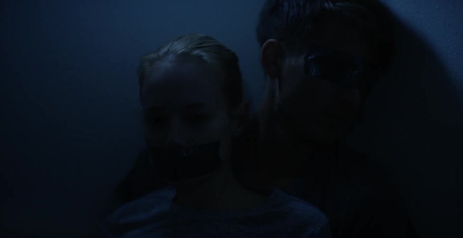 Woman and man sit with tape over their faces in a dark room