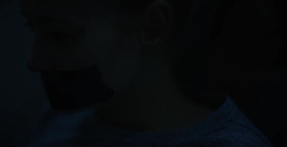 A person in the dark with their mouth duct taped