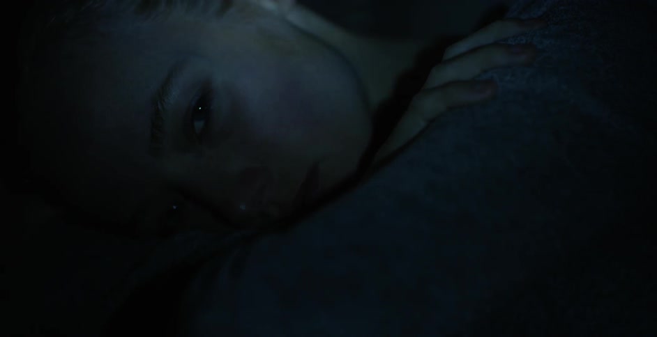 A young woman is illuminated by a flashlight while she is laying down