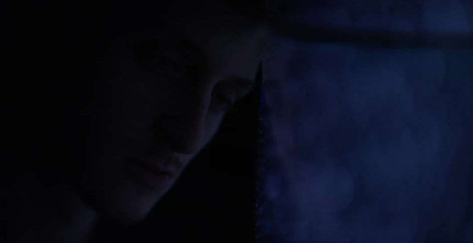 Man leans against a static riddled television set in a dark room