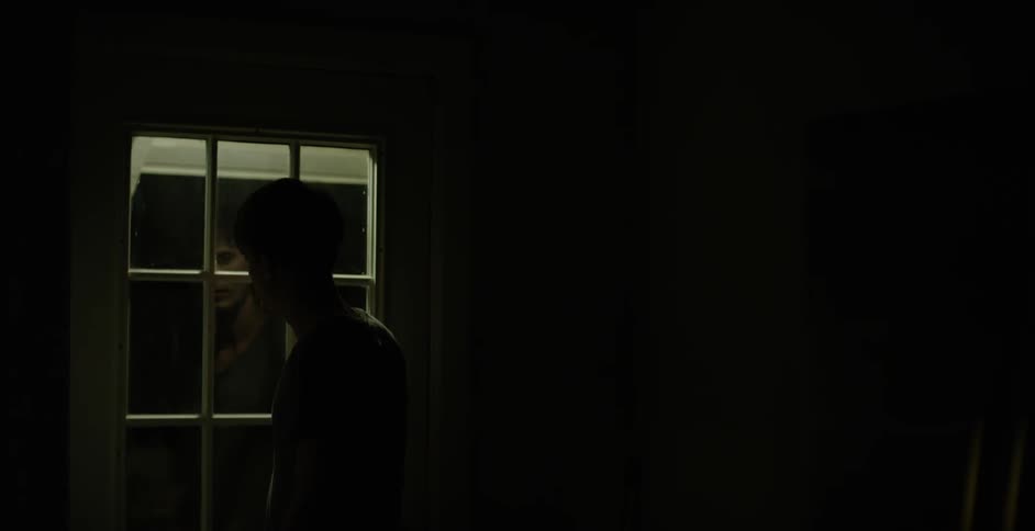 Person standing next to an exterior door in a dark room at night