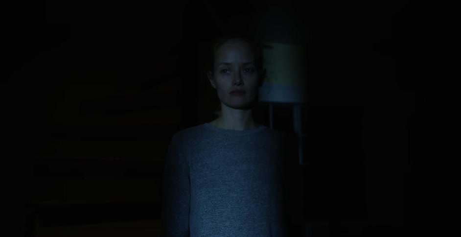 Solemn looking woman standing alone in a dark area indoors