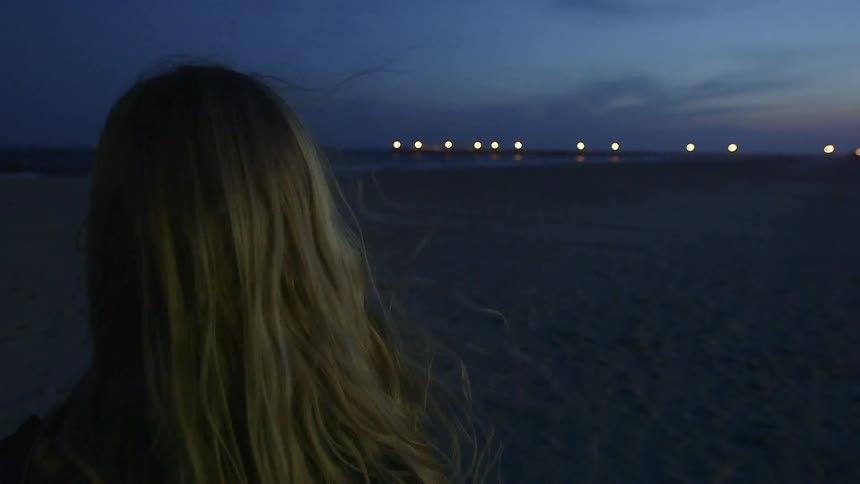A woman is standing on a wind beach at sunset