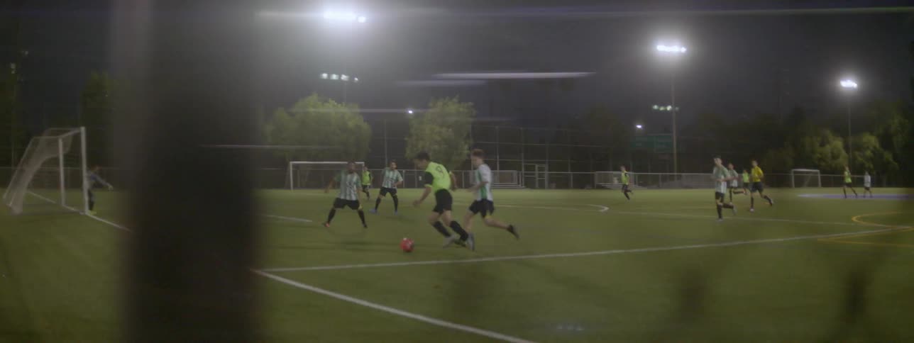 Boys play a soccer game on a field at night