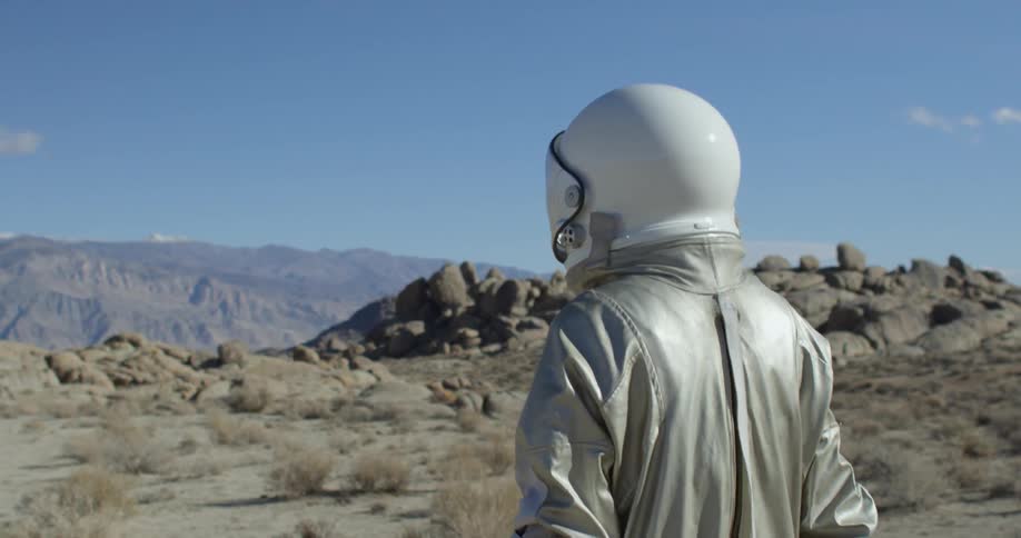 A person in a helmet and silver suit walks in the desert