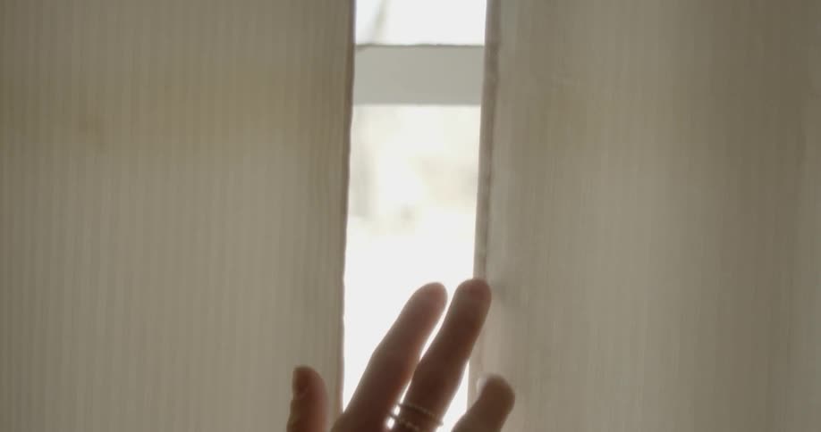 A woman rubs her hand down a pair of curtains