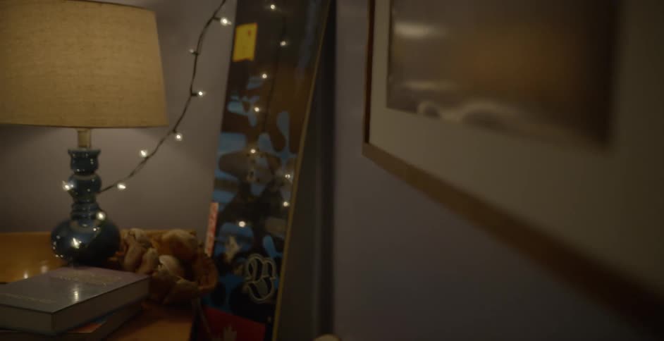 A snowboard stands in the corner of a room next to glowing strand lights