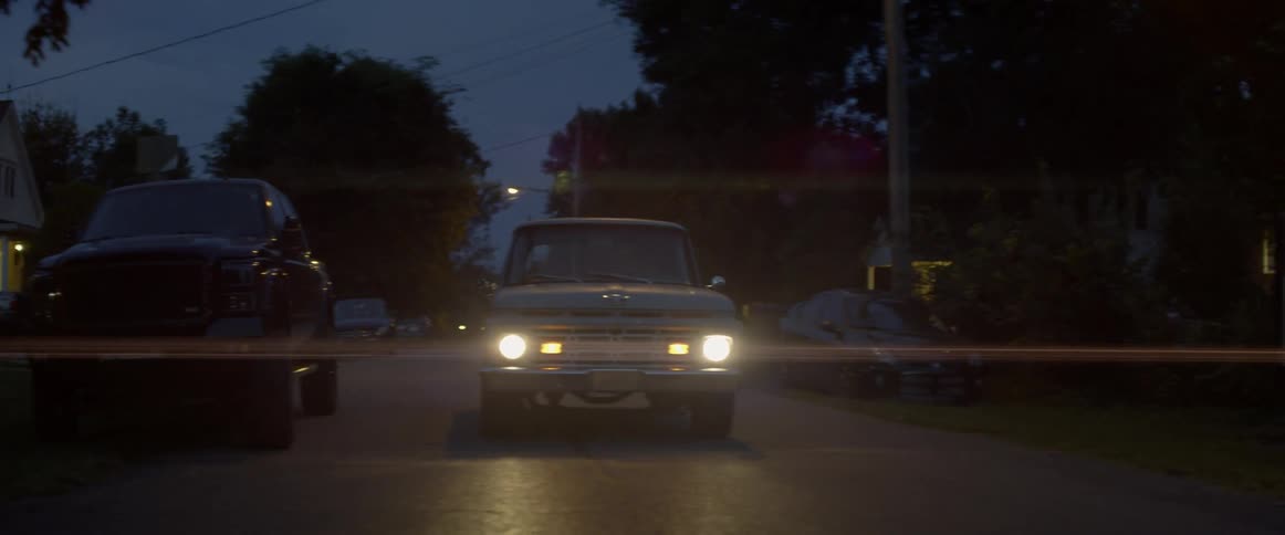 An antique truck drives on a neighborhood road at night