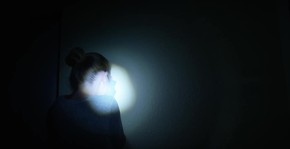 Single spot light hits a woman who is pointed towards a wall covering her face