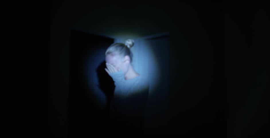 Woman stands crying in a dark room