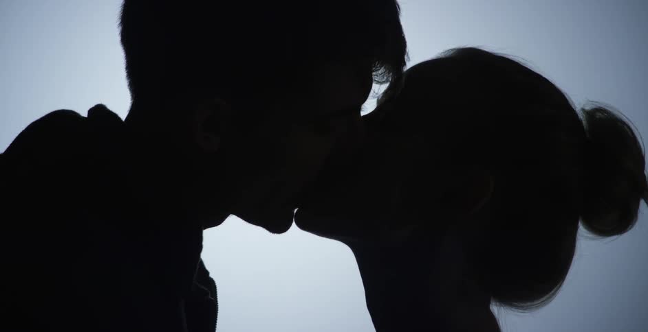 A silhouette of a young man and woman kissing