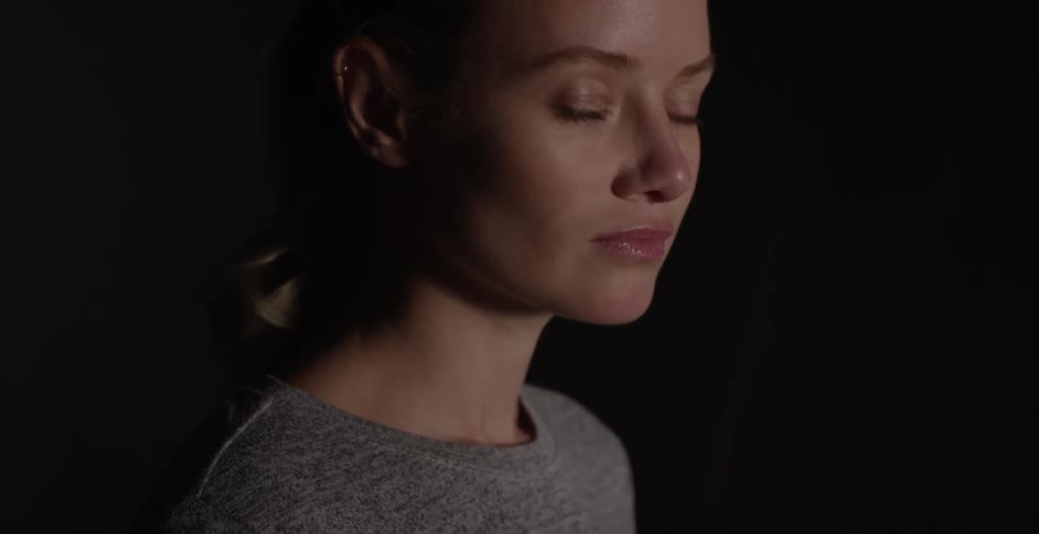 Woman standing in a dark area turns her head and opens her eyes