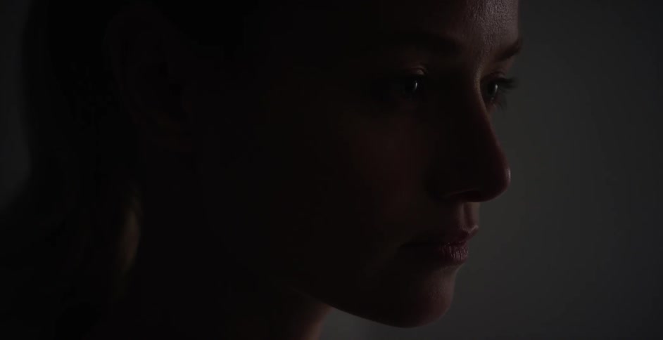 A woman in a dark room stares ahead and blinks her eyes