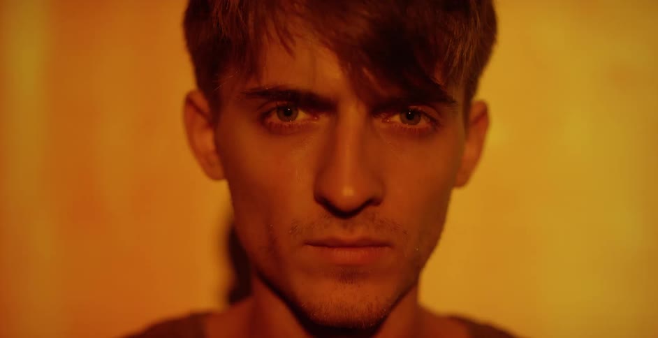 A close view of a man's face as video is being projected onto him and the wall behind him