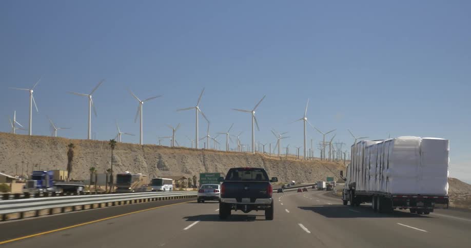 Vehicles drive on a road next to giant windmills