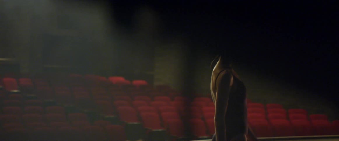 A woman in a leotard walks across a stage