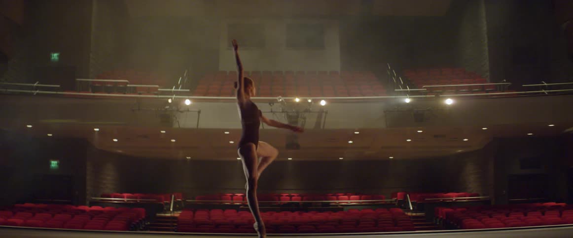 A woman dances on stage in an empty theater
