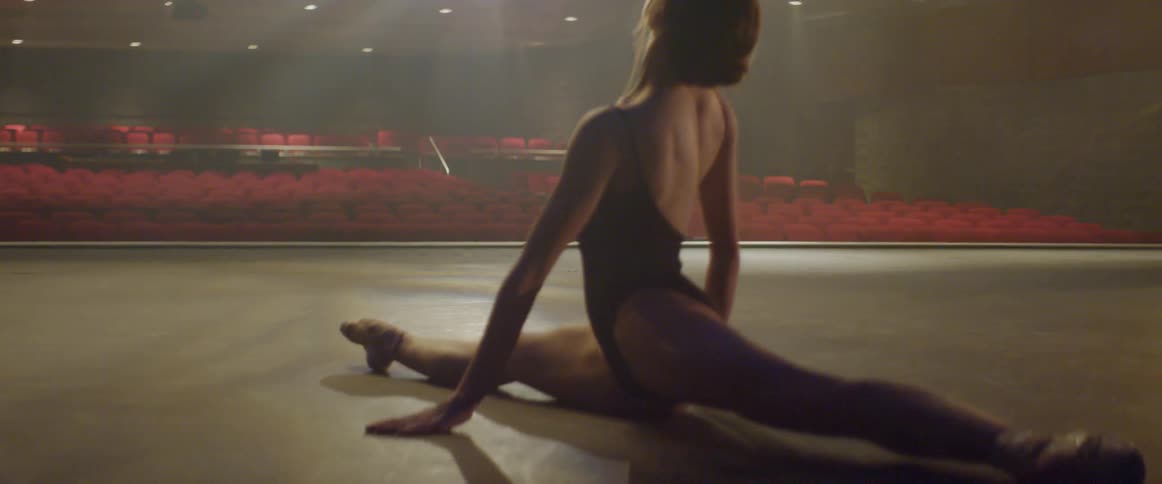 Woman does the splits on a stage in an empty auditorium