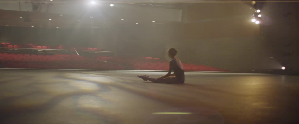 A dancer stretches on stage in an empty theater