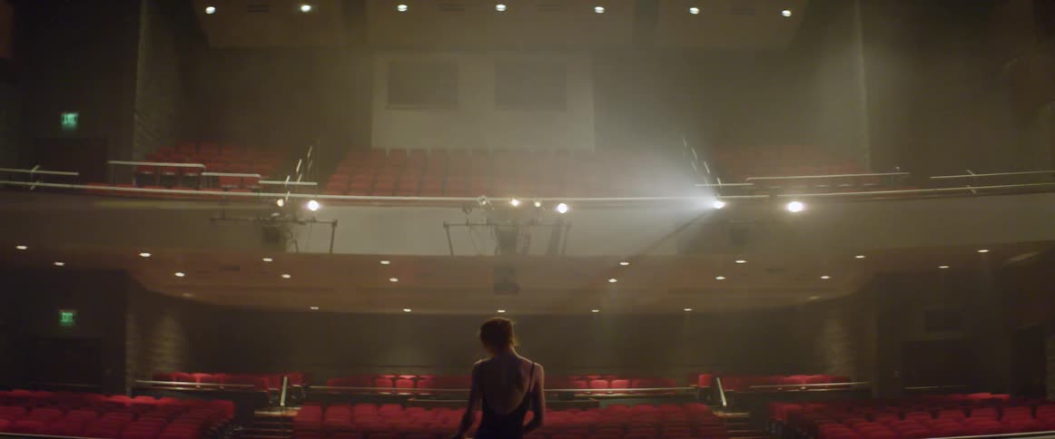 A dancer stretches on stage in an empty theater